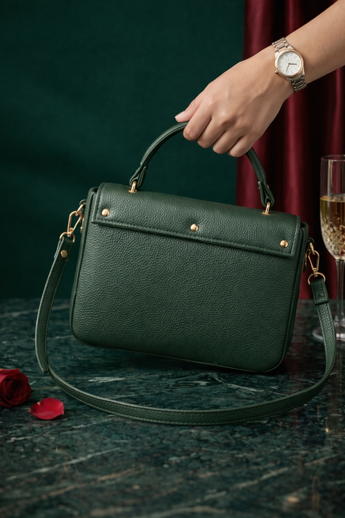 Bagistry Chic Carry handbag held by a hand with a watch, next to a glass of champagne and red rose petals on a dark surface.